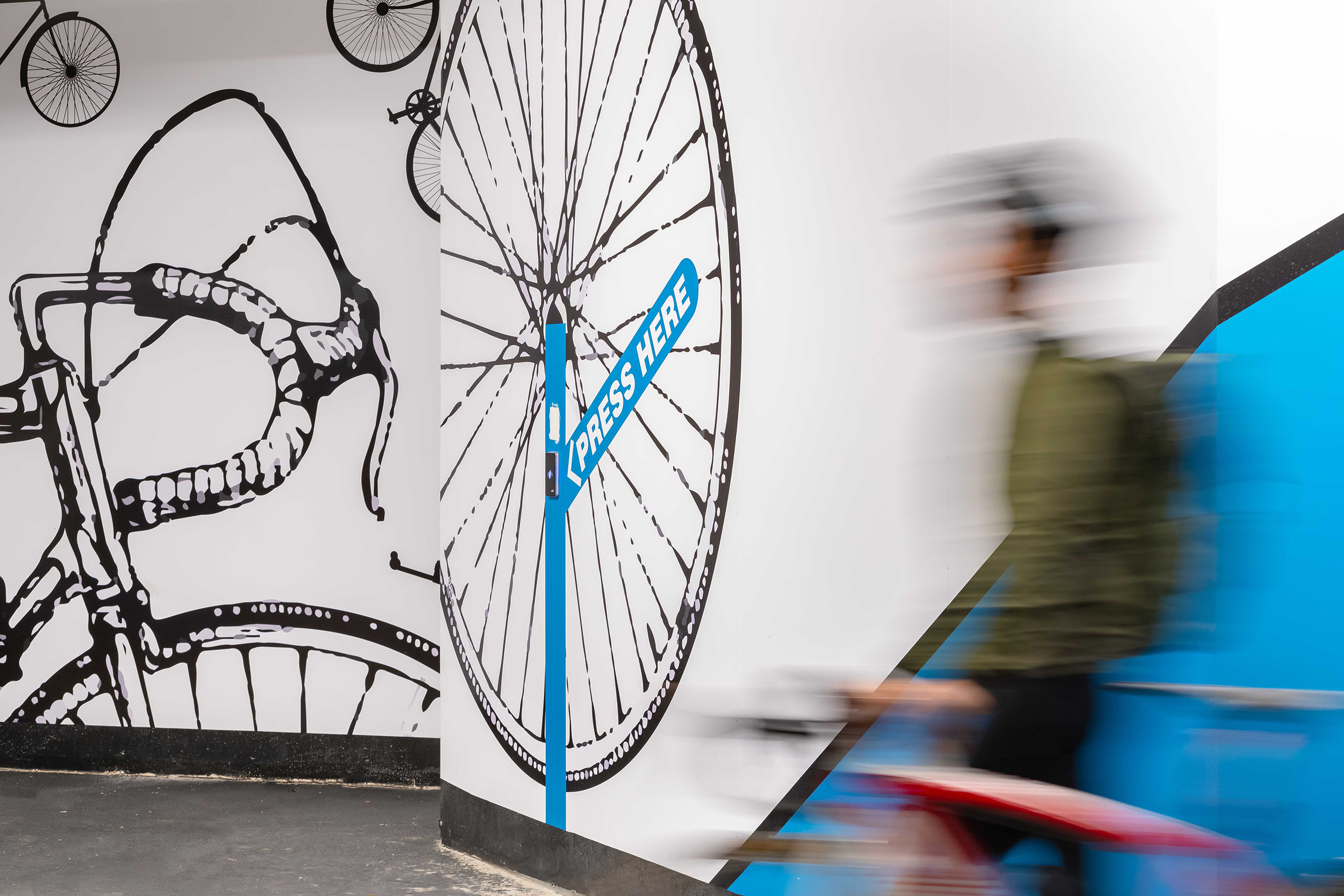 Close up of a man pushing his bike into the bicycle amenities area, adjacent to bold graphics that assist with wayfinding